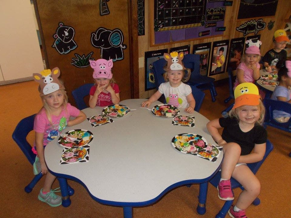 Children wearing animal hats sitting at a table with plates