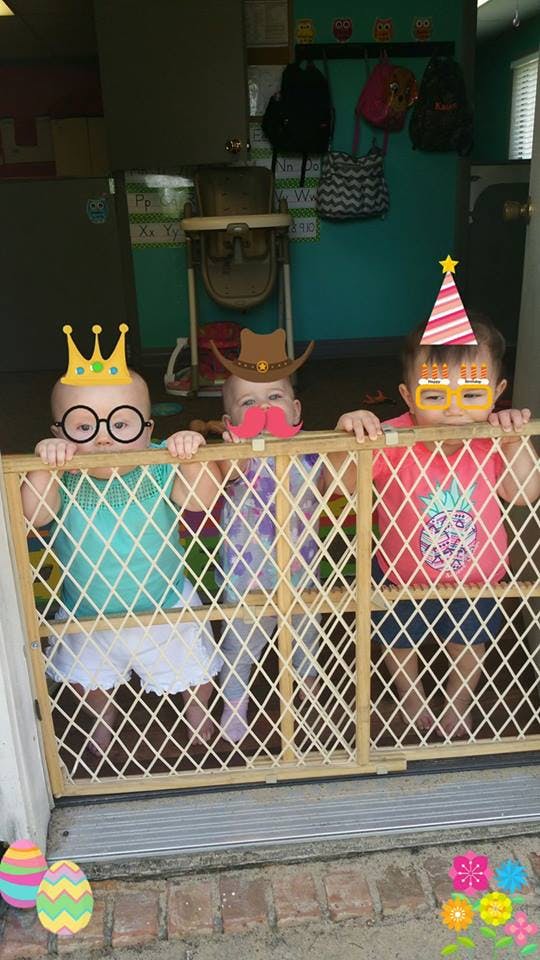 Three children behind a baby gate with digital stickers of hats, glasses, and mustaches