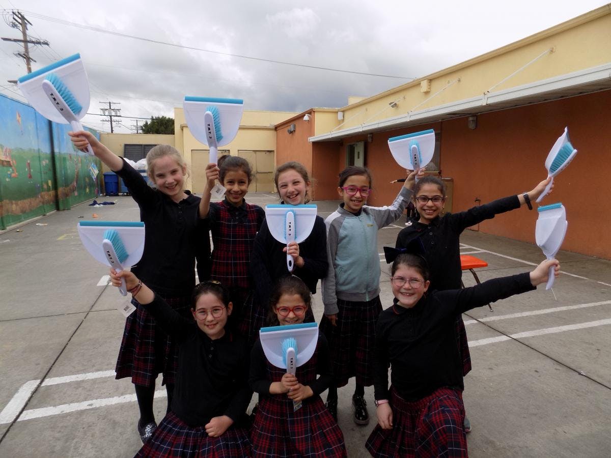Group of children holding up dustpans with brushes