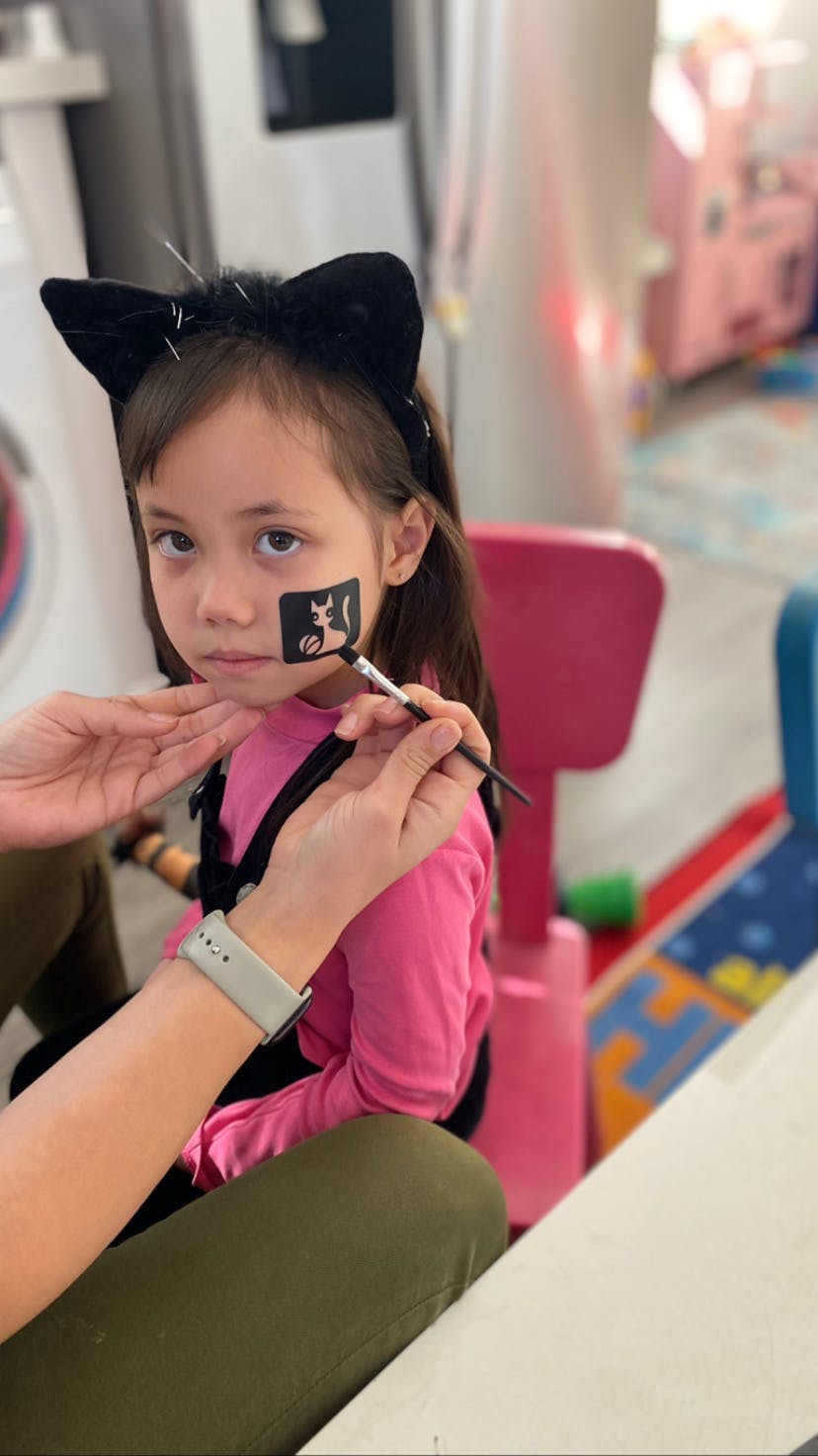 Child with cat ears getting face painted with a cat design
