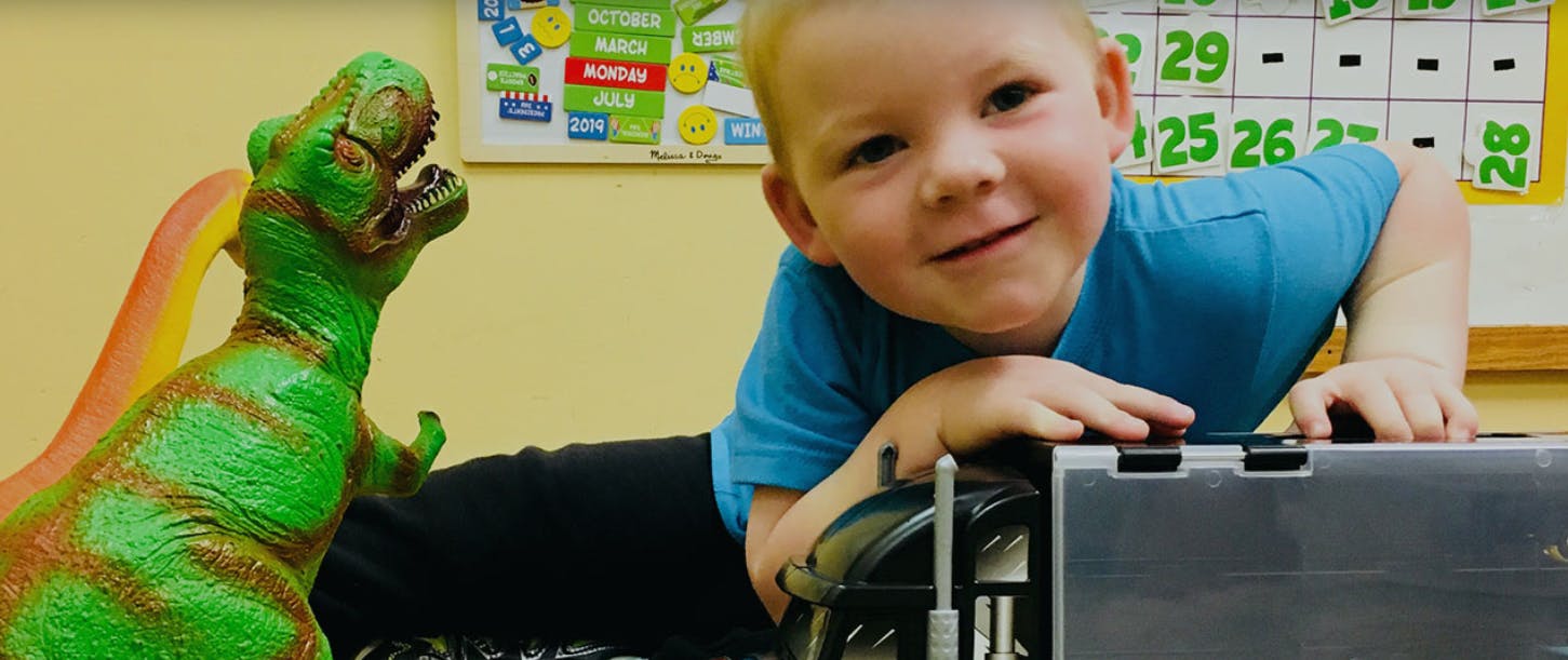 Child looking over a laptop with a dinosaur toy