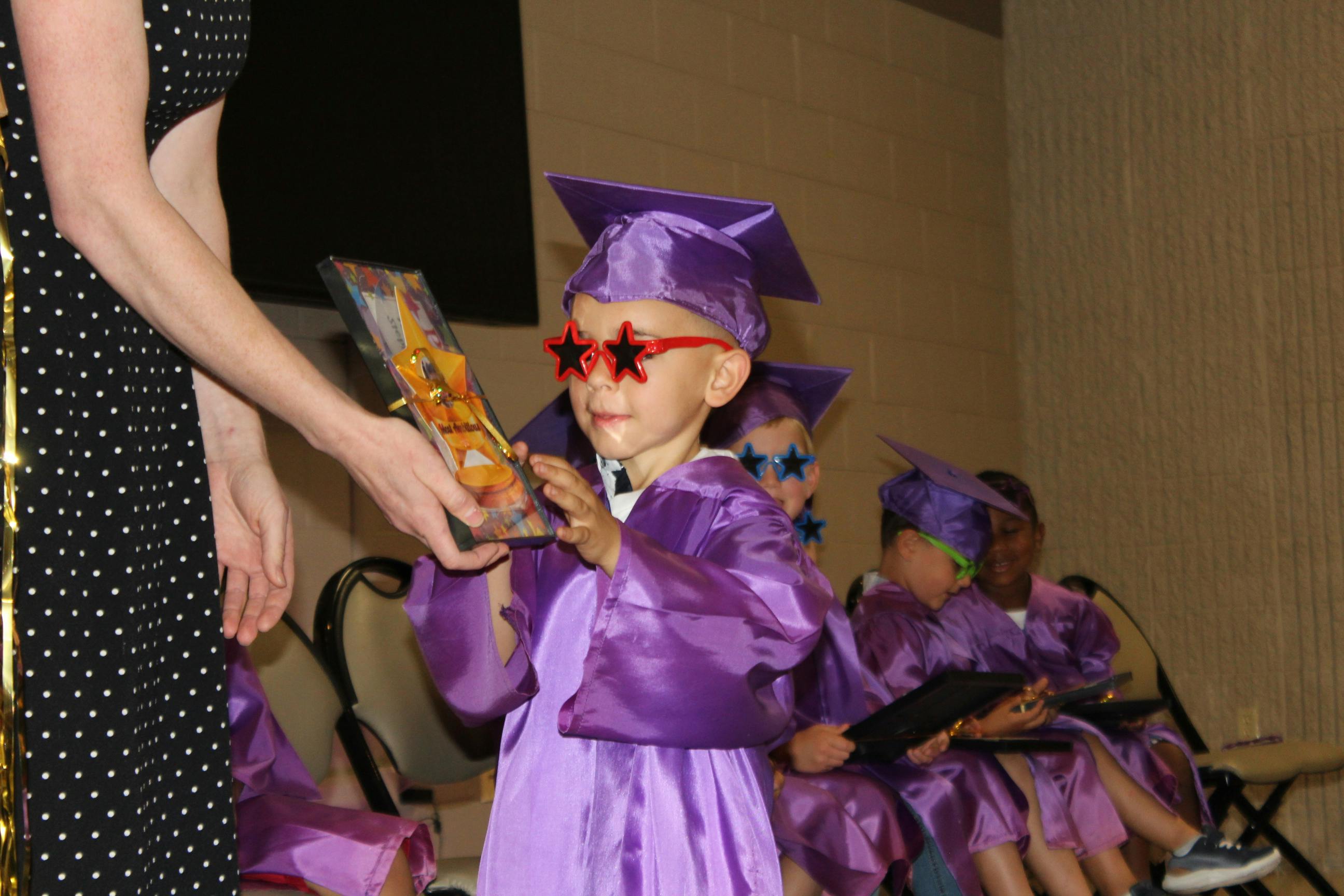 Child in graduation cap and gown receiving an item from a person
