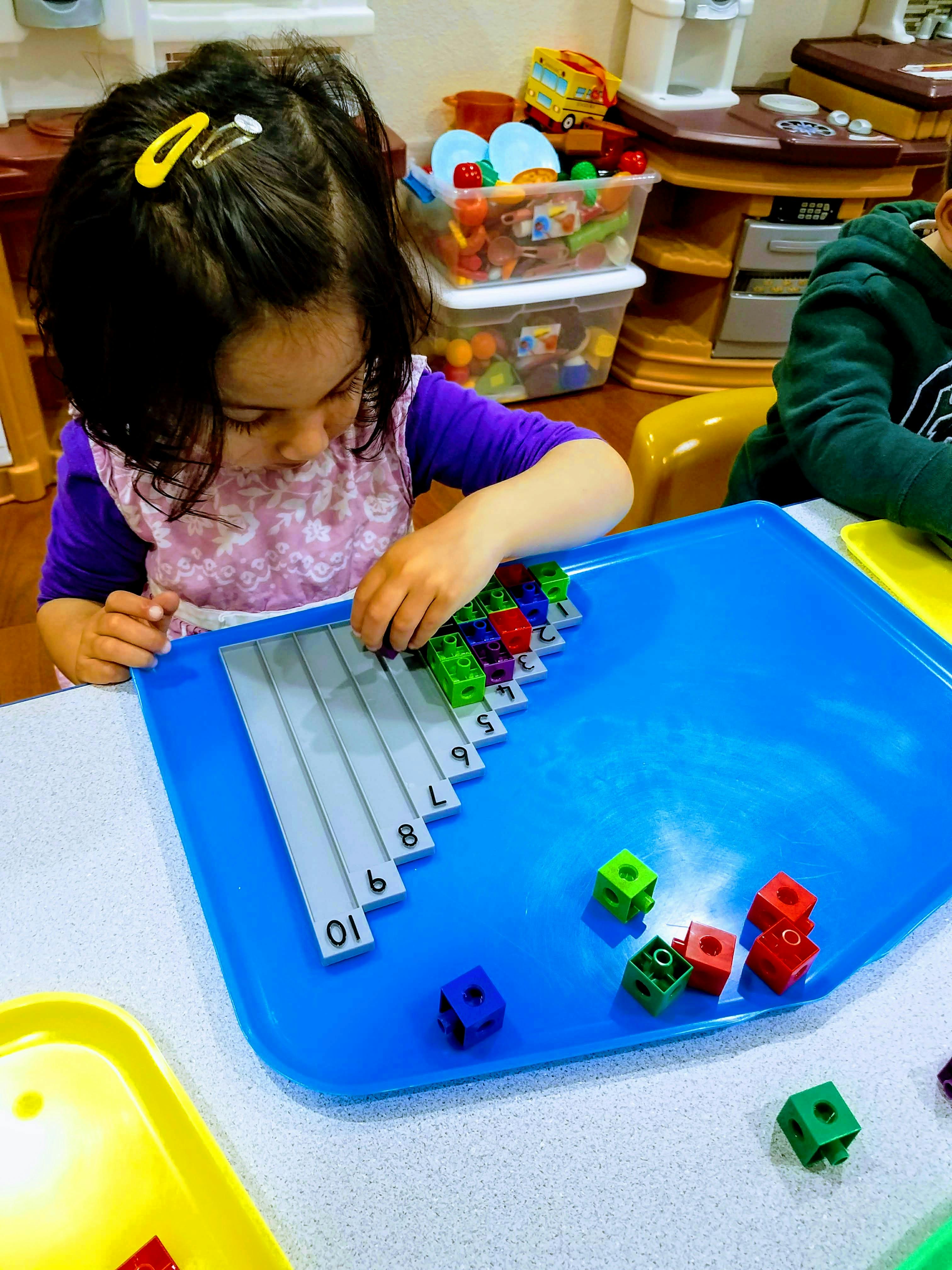 Child playing with colorful connecting cubes on a numbered tray