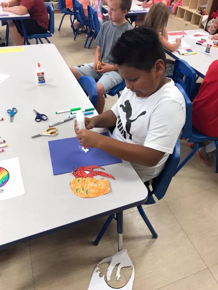 Child gluing paper cutouts onto blue paper in a classroom