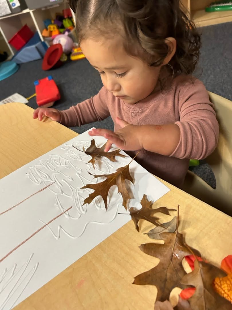 Child gluing dried leaves onto paper at a table