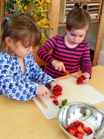 Two children cutting strawberries on a table