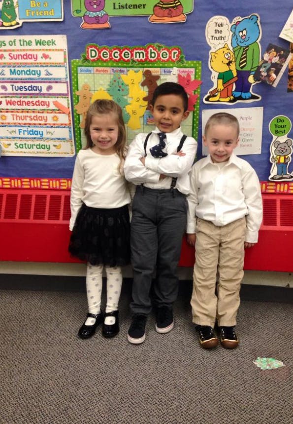 Three children standing in front of a classroom calendar for December