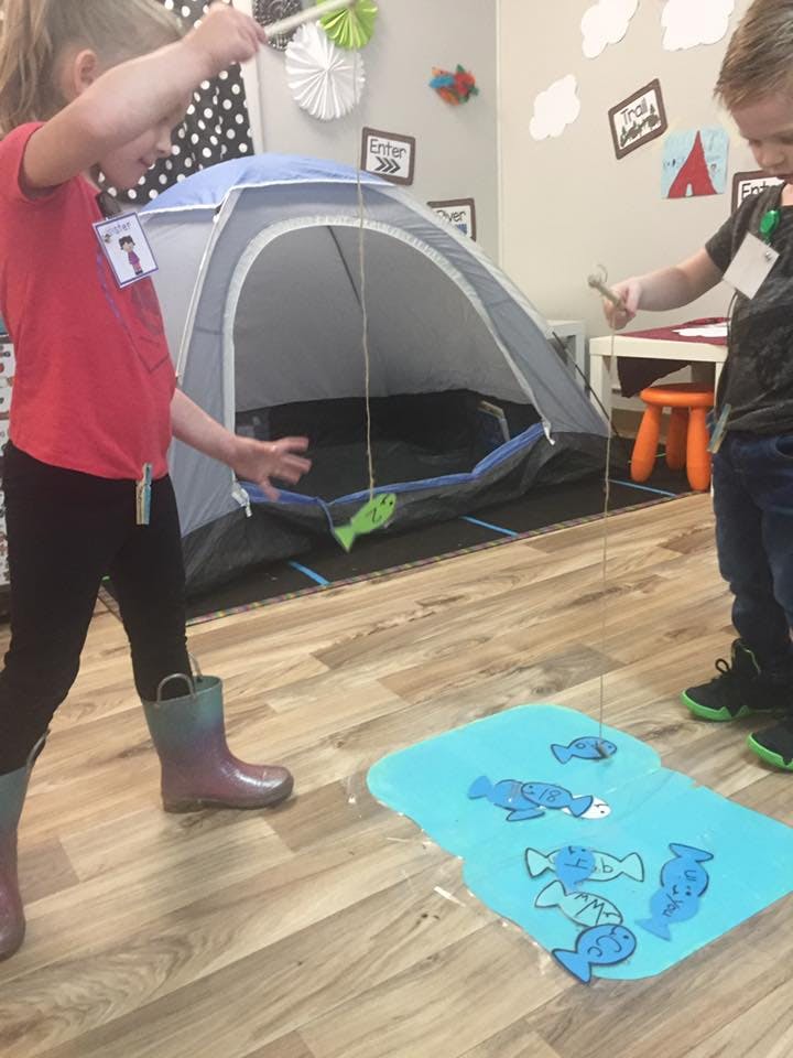 Two children playing with fishing rods and fish cutouts in a classroom