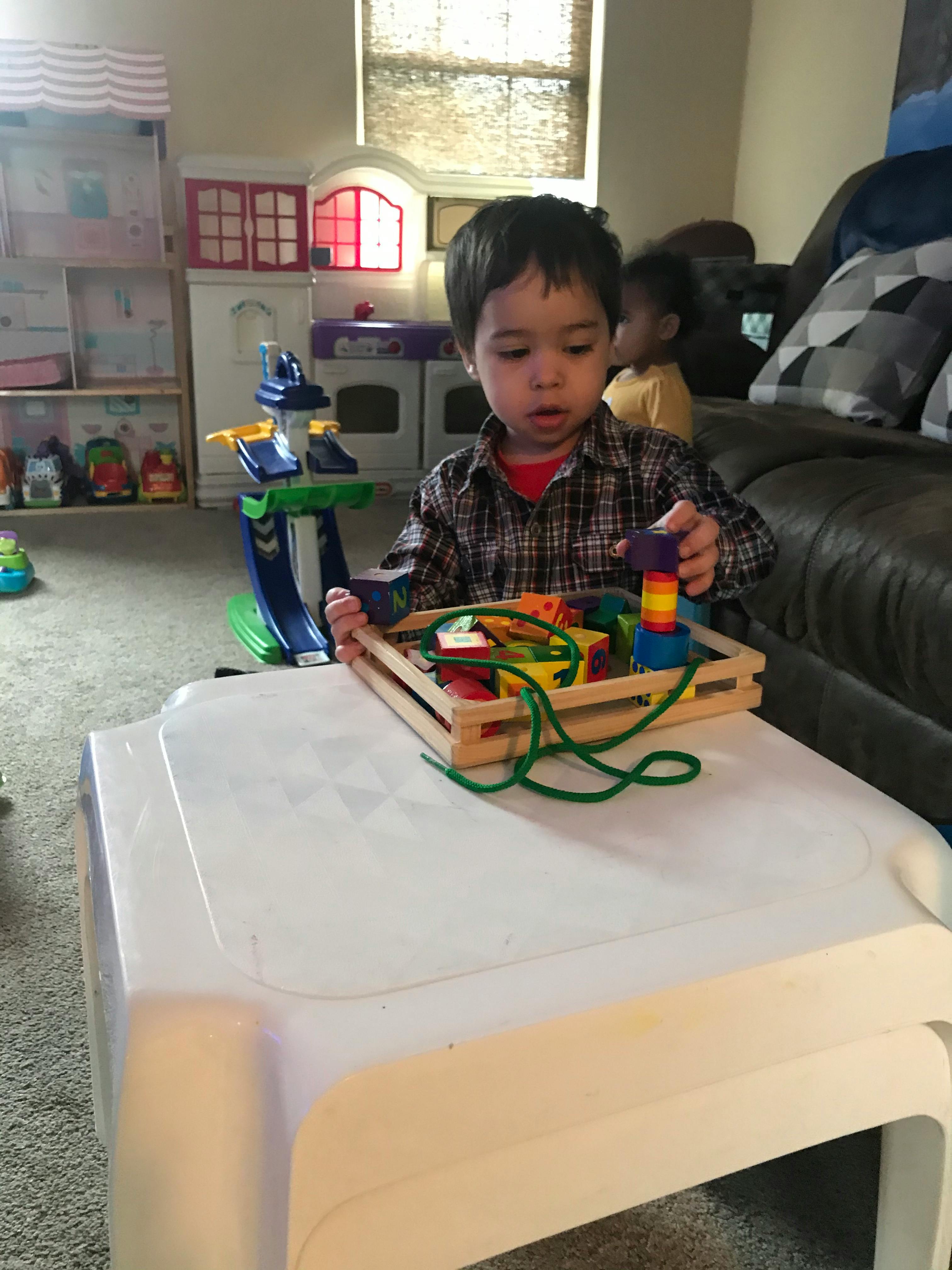 Child playing with a wooden lacing toy on a white table