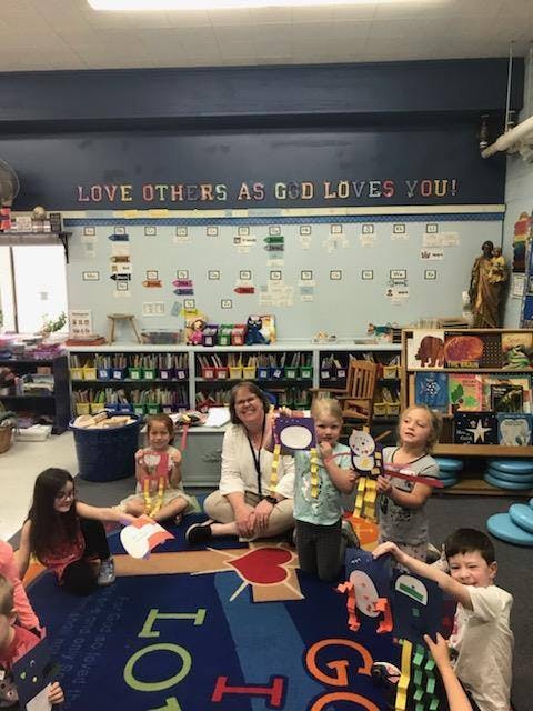 Adult and children sitting on a rug in a classroom with crafts