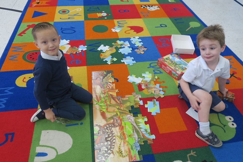 Two children on a colorful rug with a large puzzle