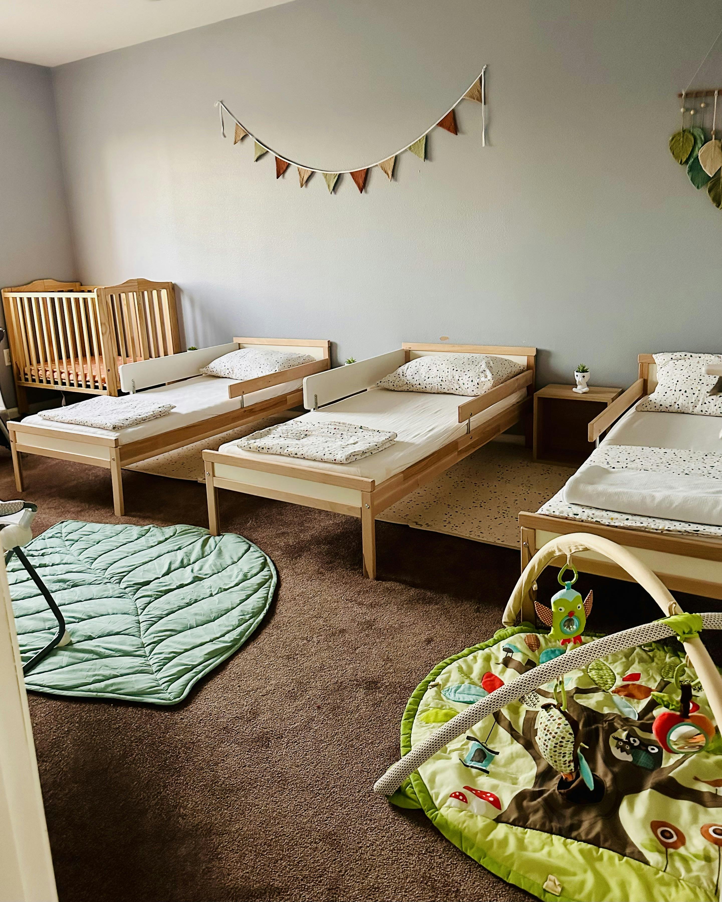 Children's room with several toddler beds, a crib, and playmats on the floor