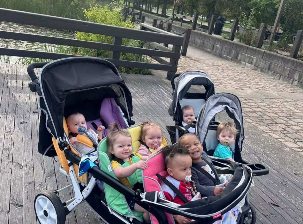 Seven infants and toddlers in strollers on a boardwalk
