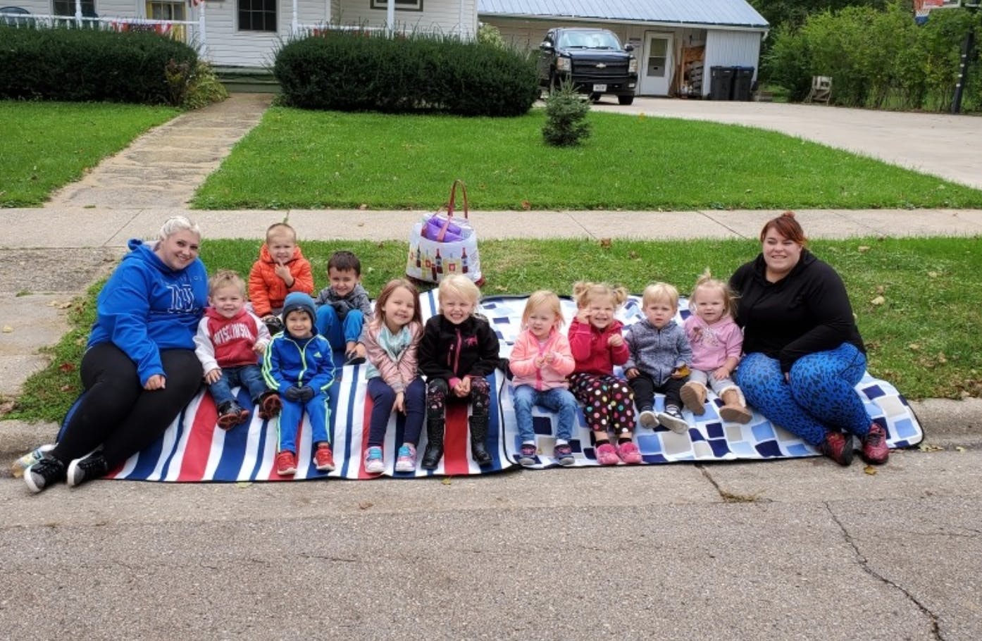 Two adults and multiple children sitting on blankets on a sidewalk