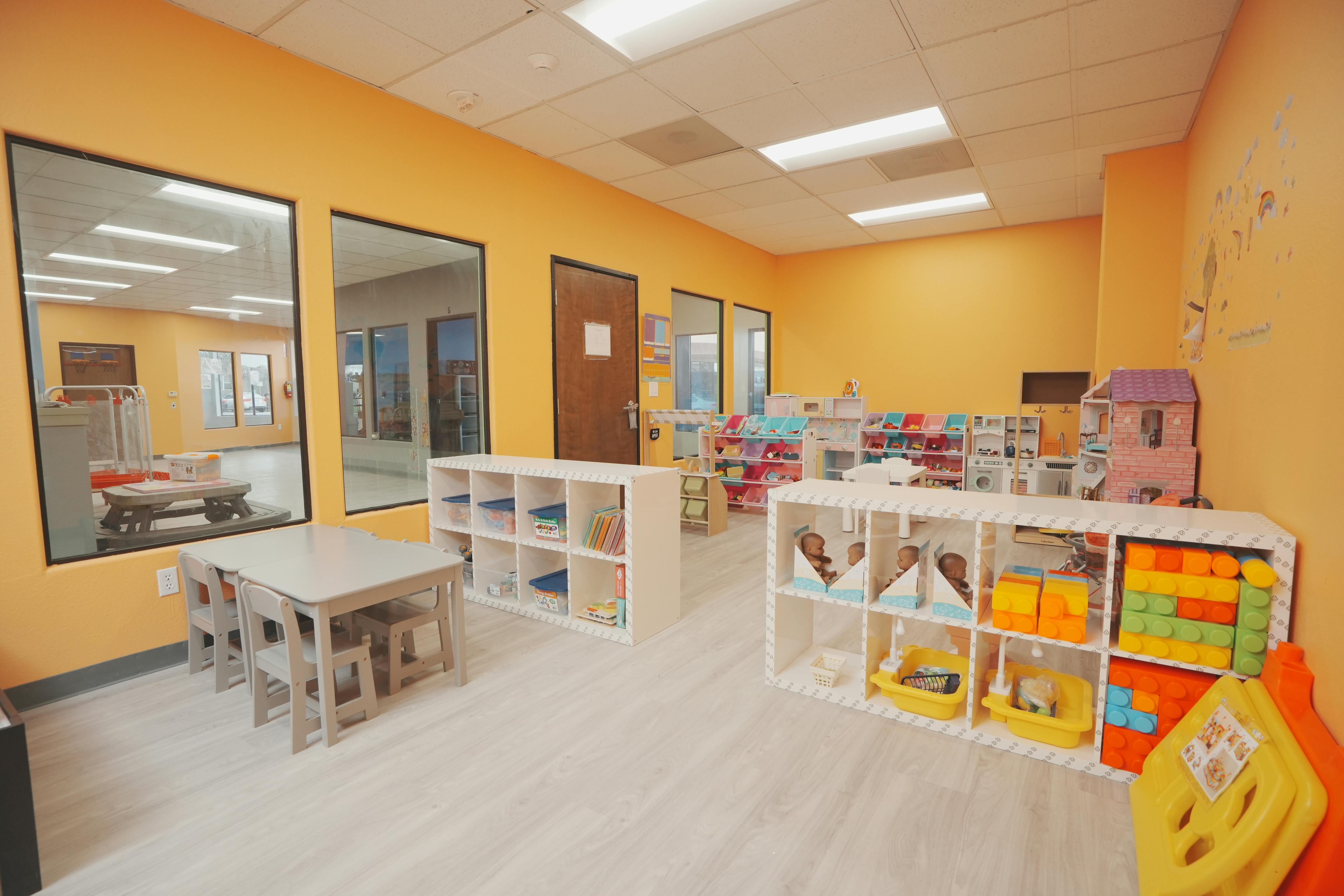 Classroom with small tables and chairs, shelves with toys and supplies