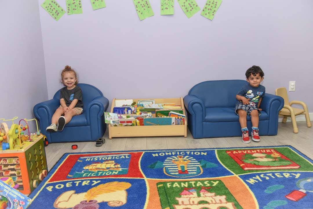 Two children sitting on blue chairs in a classroom