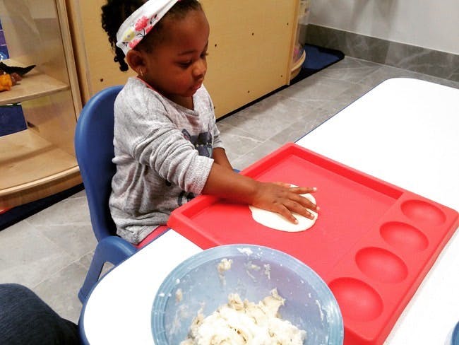 Child pressing dough on a red tray