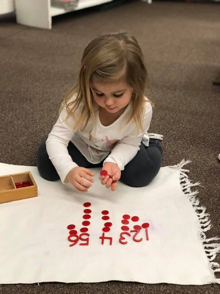 Child playing with red number and dot counters on a white mat
