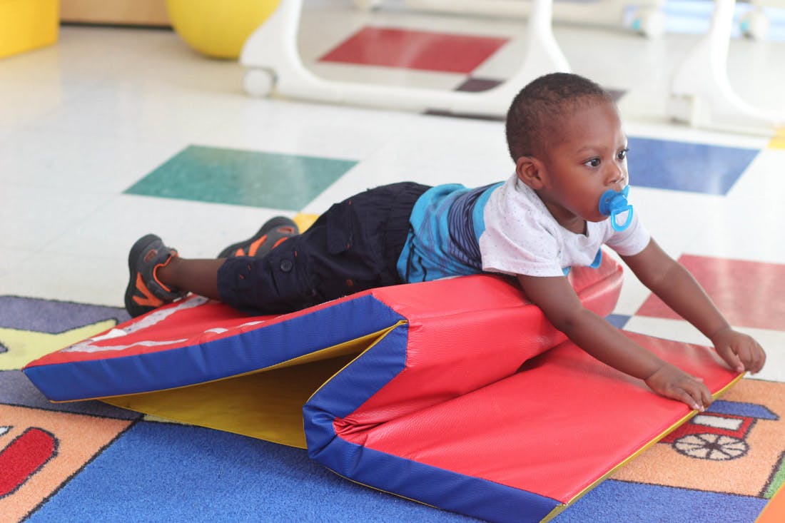 Child with pacifier lying on red and blue soft play equipment