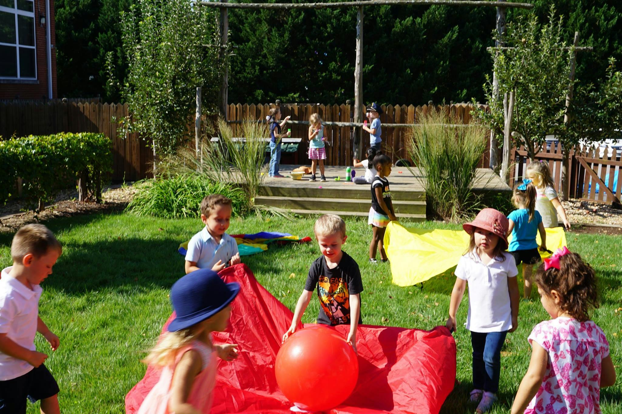 Children playing with a large red ball and fabric on a grassy lawn