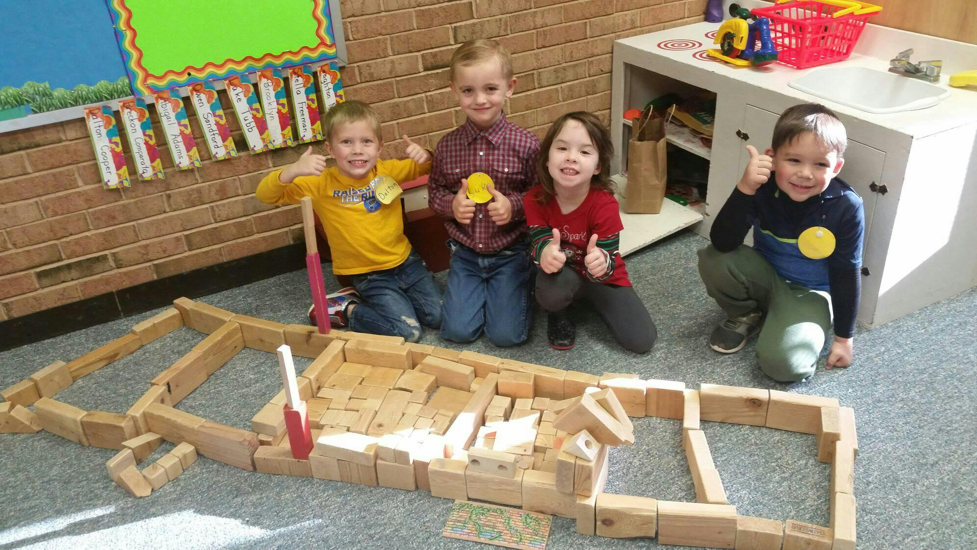 Four children with a wooden block structure in a classroom