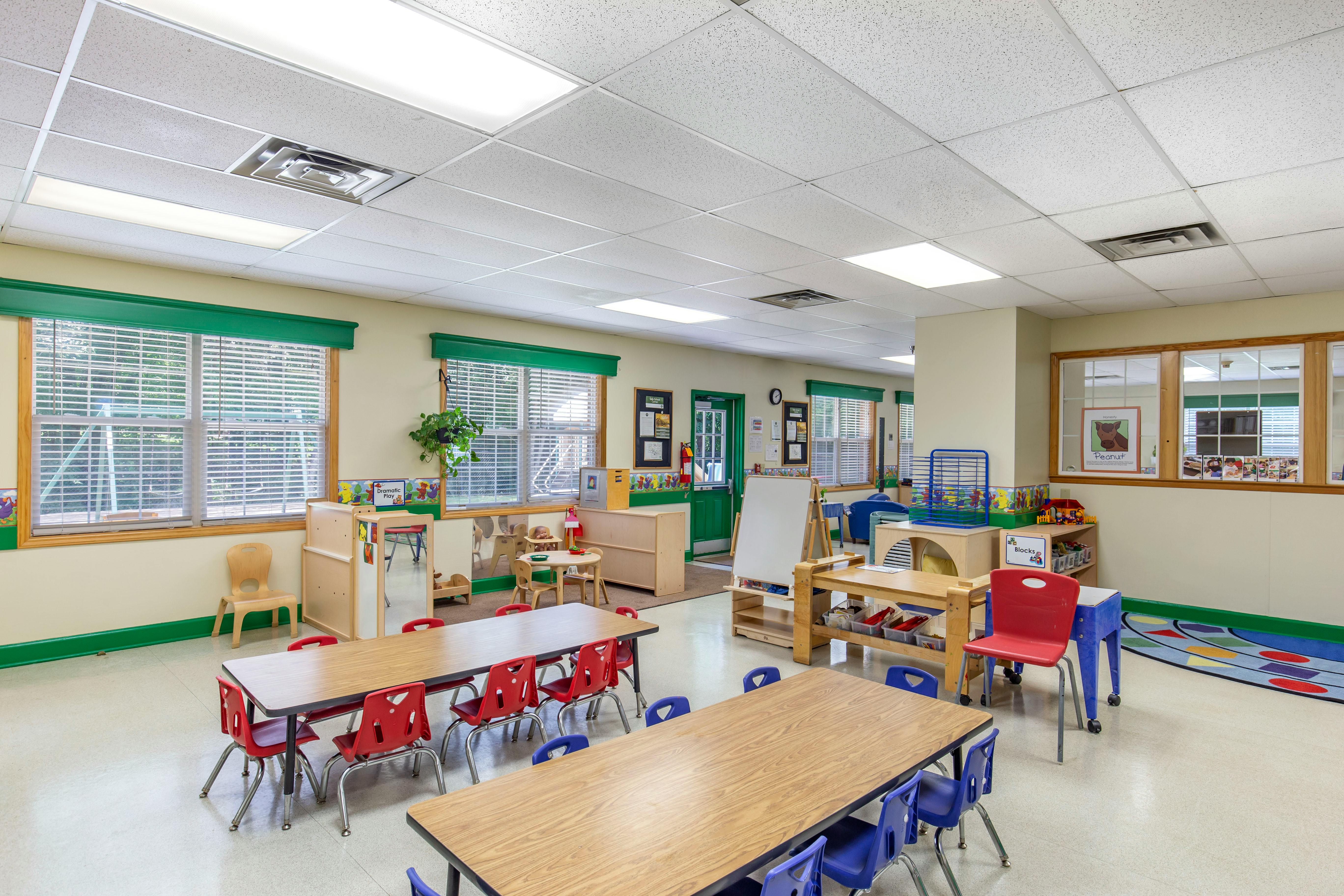An empty classroom with several tables and chairs, play areas, and large windows