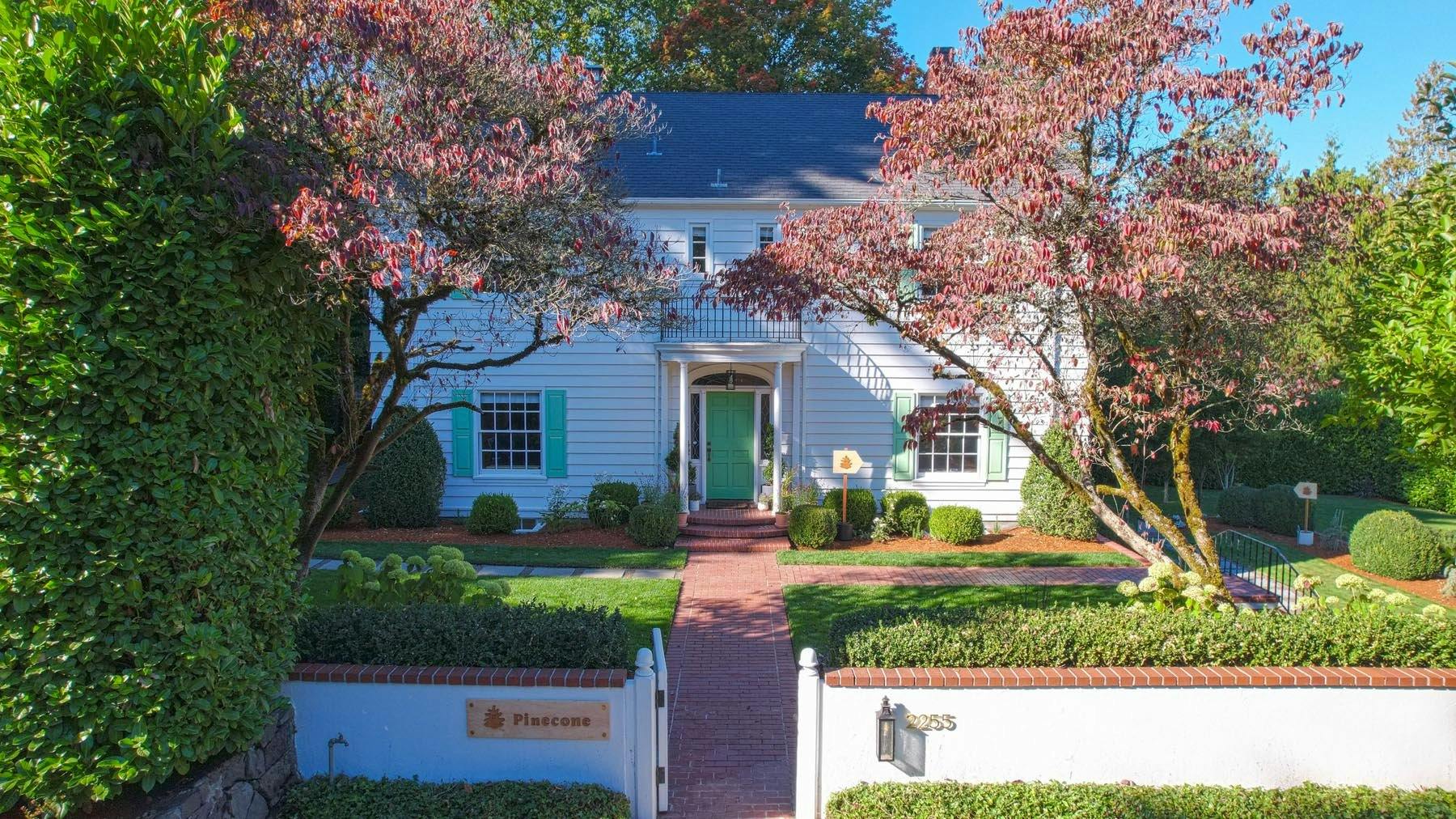White house with green door and shutters, surrounded by trees with pink leaves