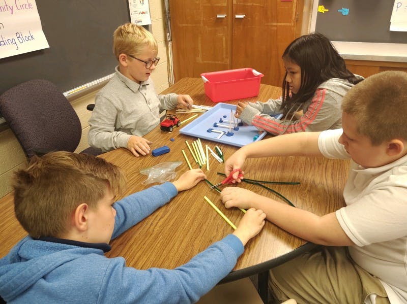 Four children at a table working on a craft project with pipe cleaners and straws