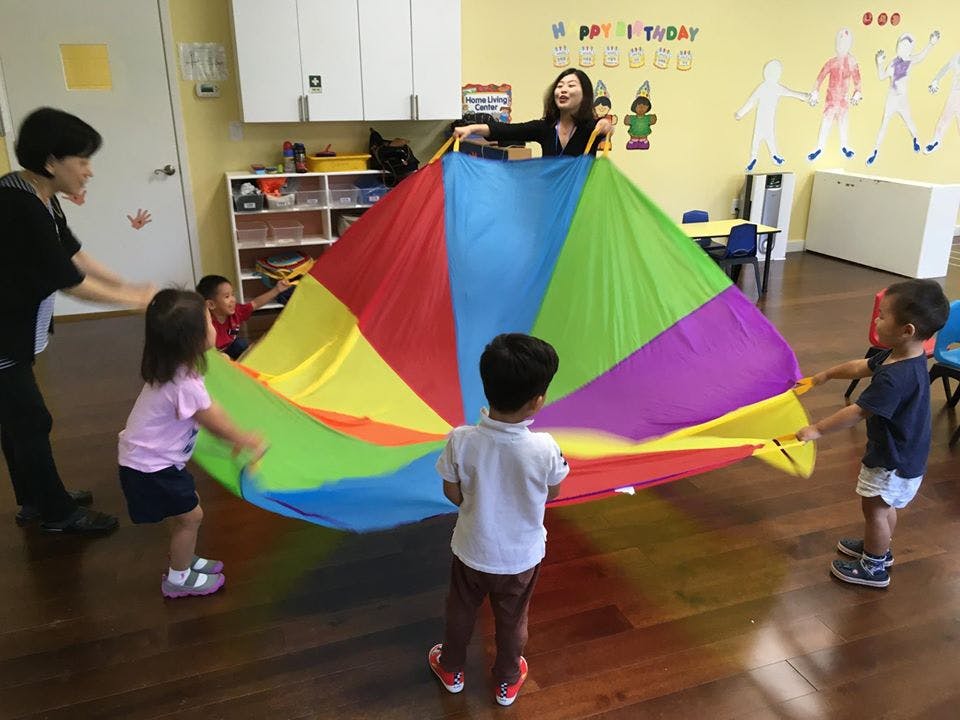 Adults and children playing with a colorful parachute in a classroom
