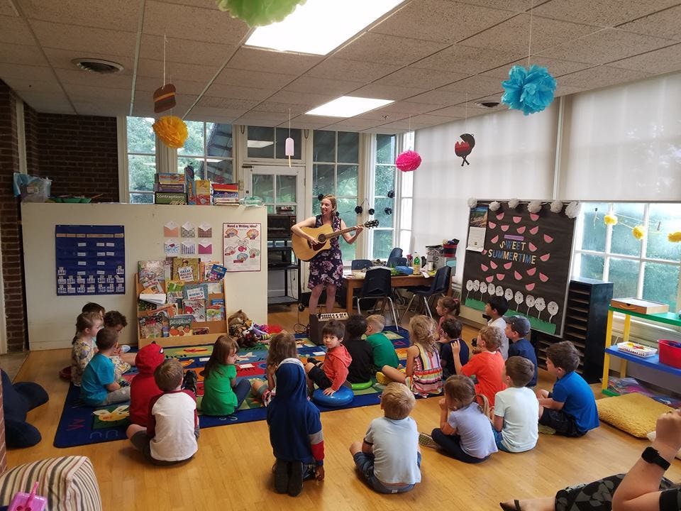 Person playing guitar for a group of children sitting on the floor