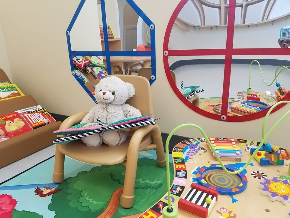 Teddy bear sitting on a chair with an open book in a play area