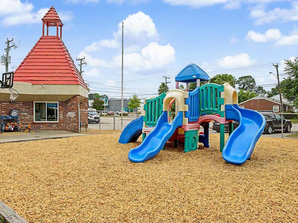 A colorful playground set with slides and a red-roofed building on a wood chip surface