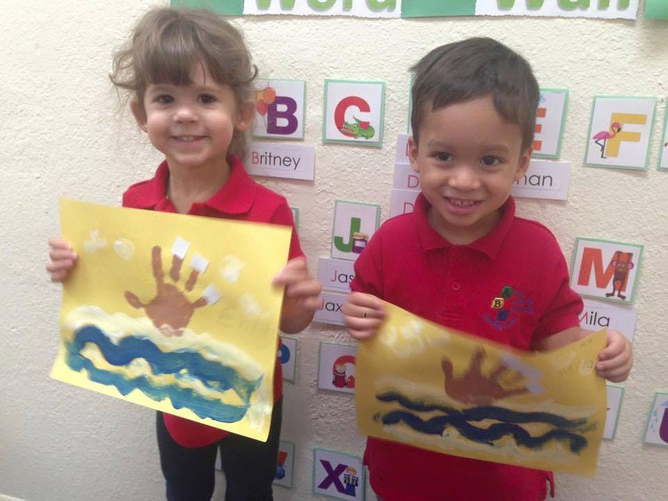 Two children holding up artwork with handprints and blue waves