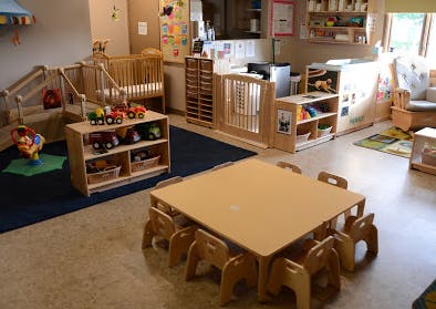 Daycare room with cribs, play area, and small table with chairs
