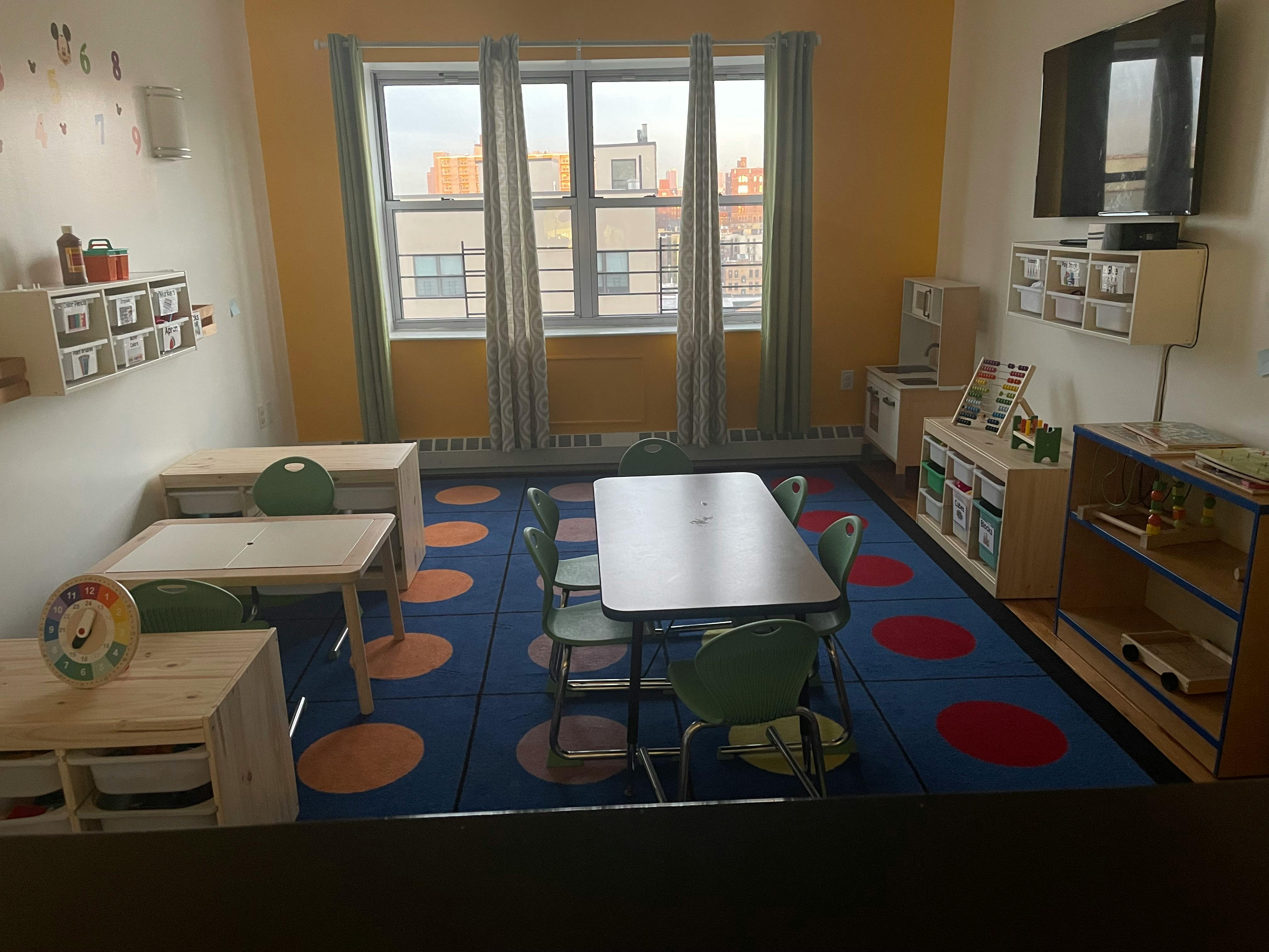 Classroom with small tables and chairs, shelves, and a television