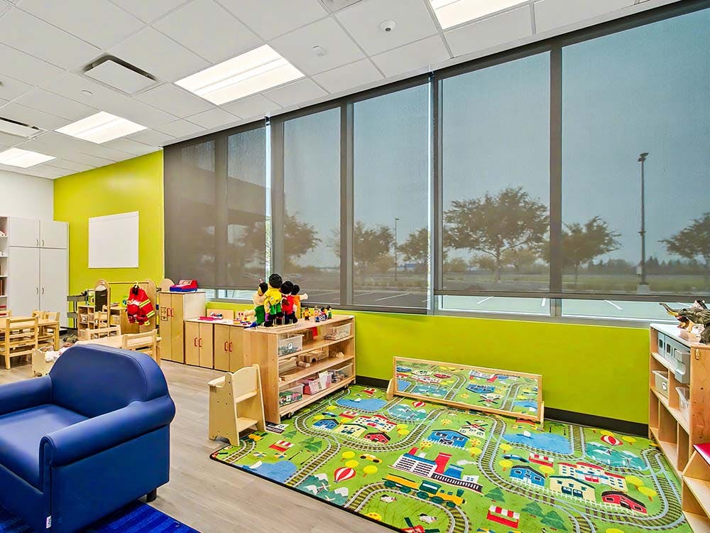 Classroom with toy storage, small chairs, and a playmat with roads