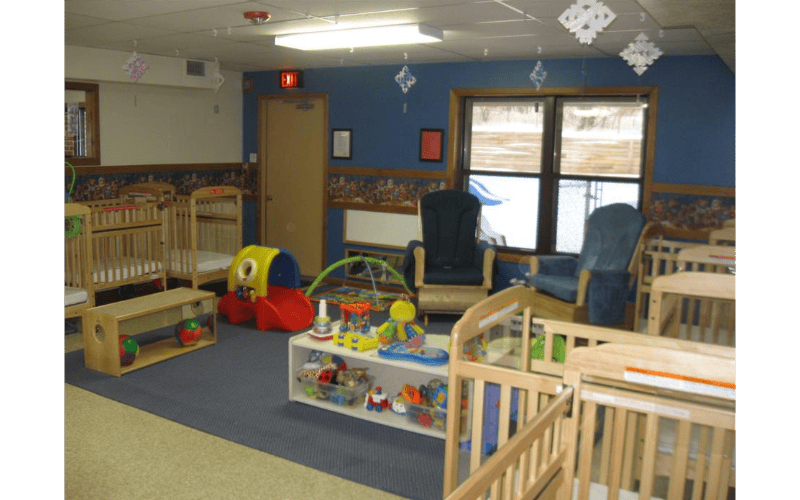 An empty nursery room with multiple cribs, a red and yellow slide, and toys