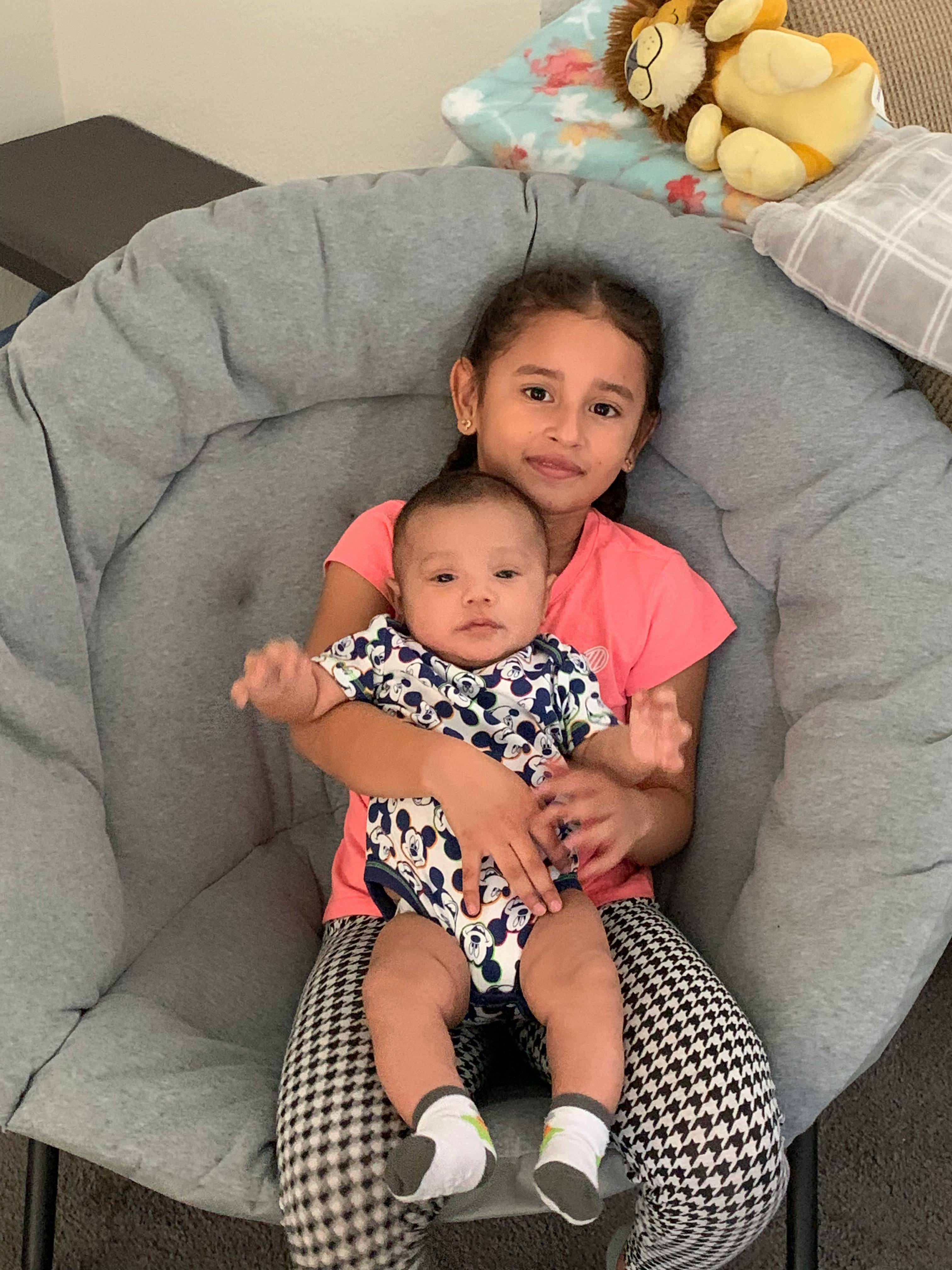Child holding an infant on a gray chair