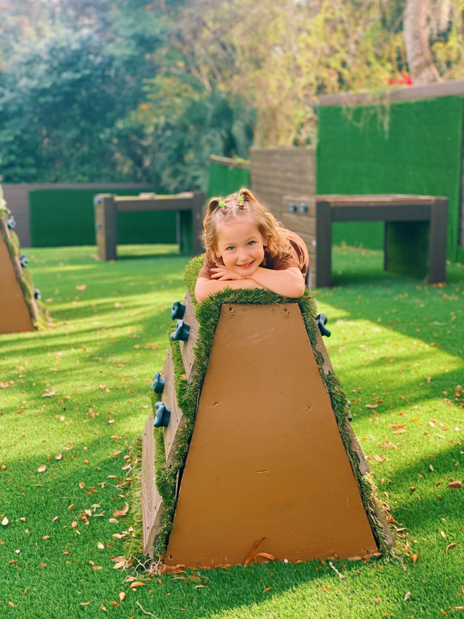 Child resting on a climbing structure in a grassy area