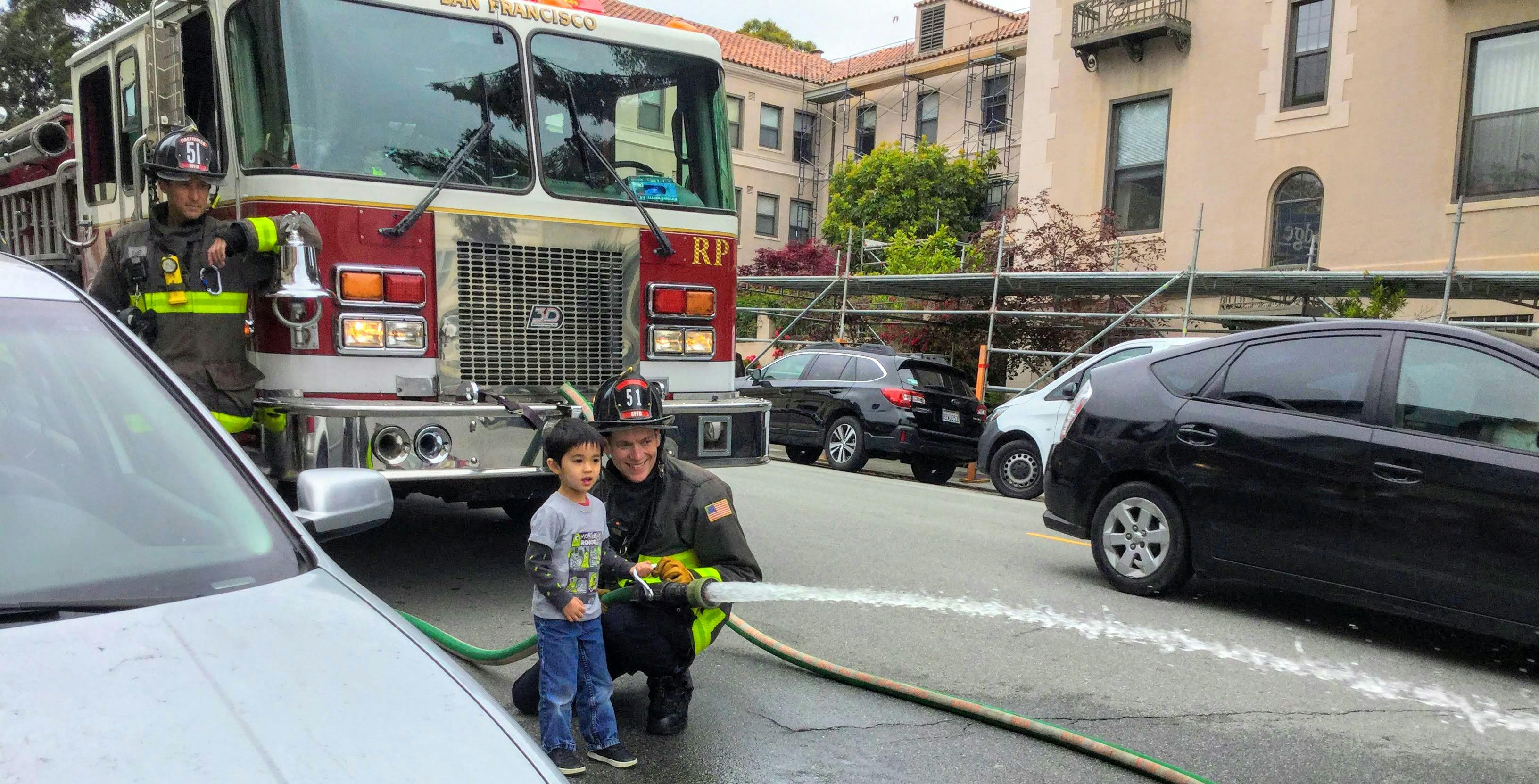 Firefighter and child holding a hose with water spraying from it
