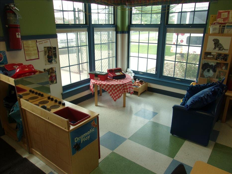 Dramatic play area with toy kitchen, table with cash register, and windows