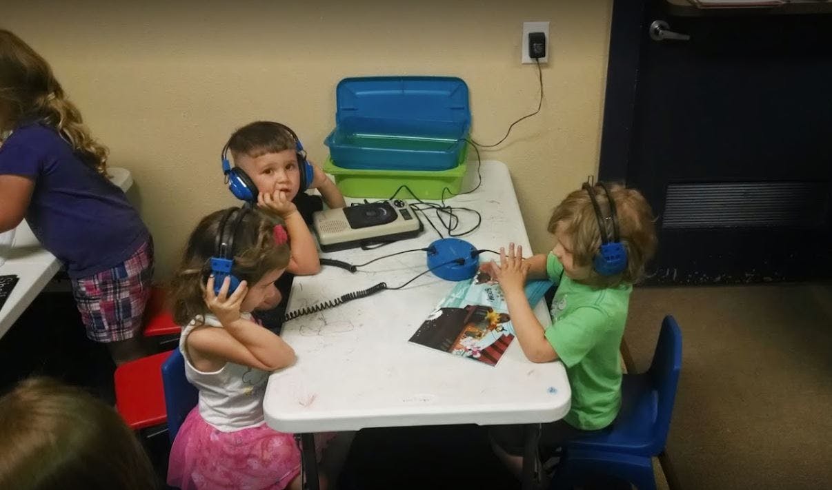 Three children wearing headphones at a table