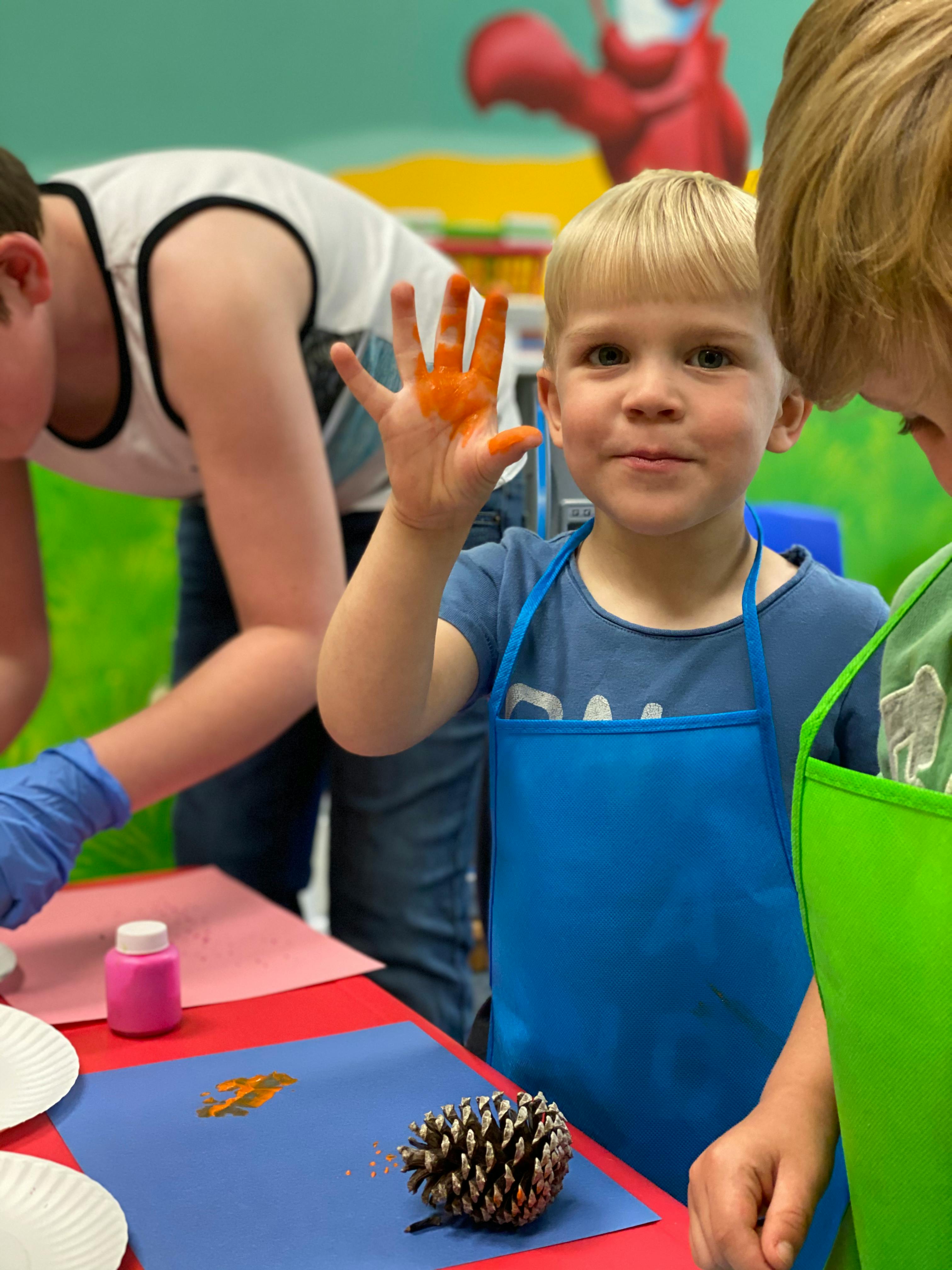 Child in blue apron with painted hand, another person in background