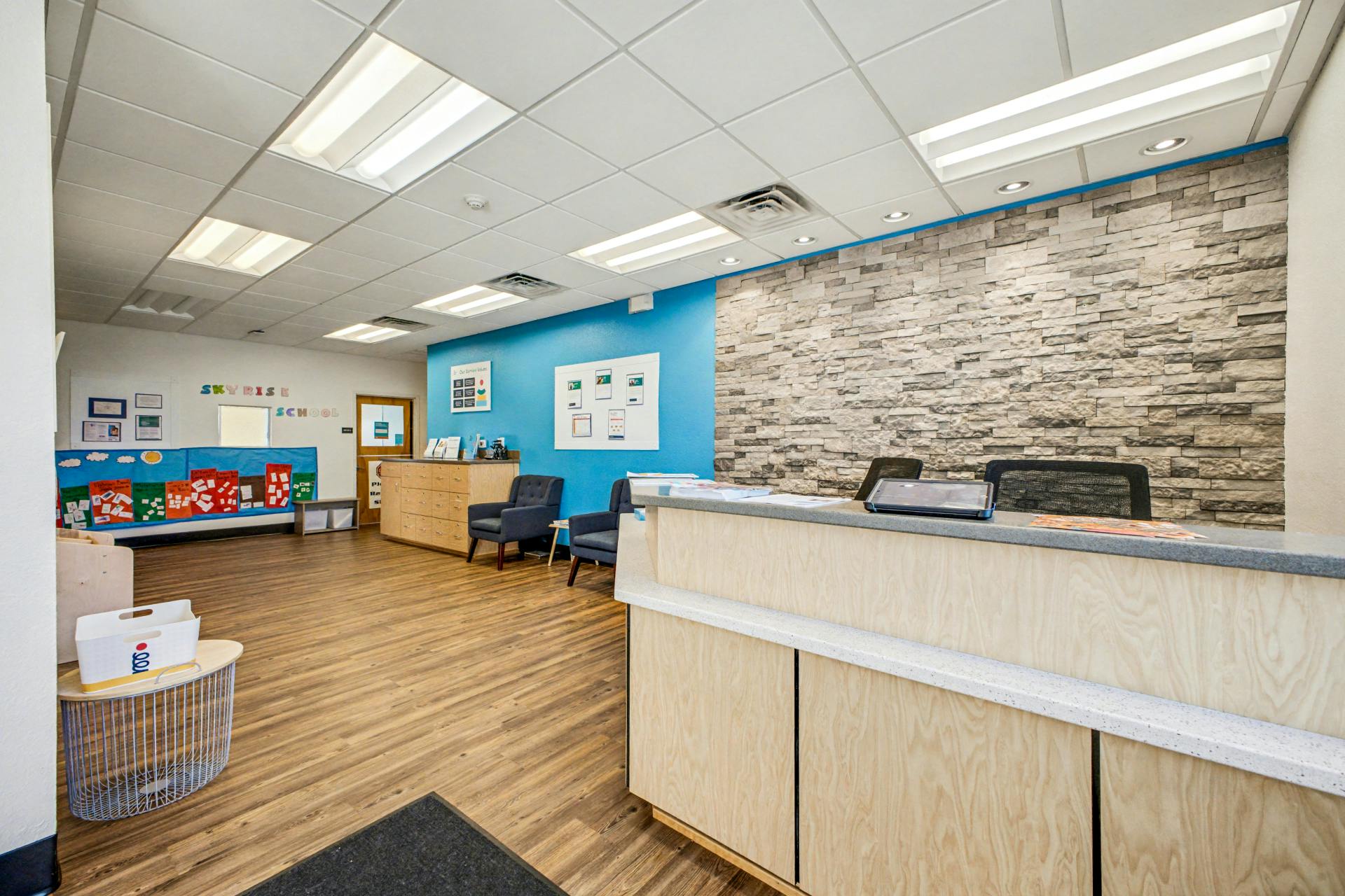 Reception area with a light wood desk, blue wall, and brick accent wall