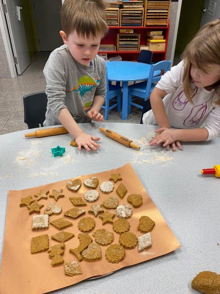 Two children making cookies with cookie cutters and rolling pins