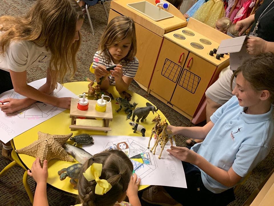 Children playing with animal figurines and drawing at a yellow table
