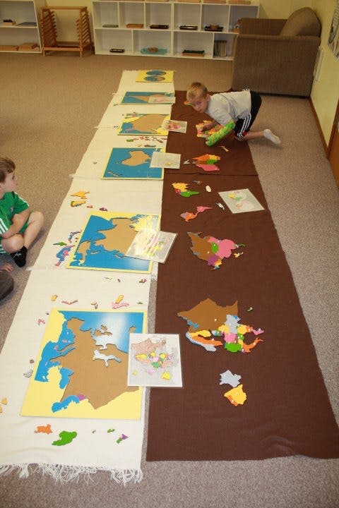 Child on floor assembling a large map puzzle with another child nearby