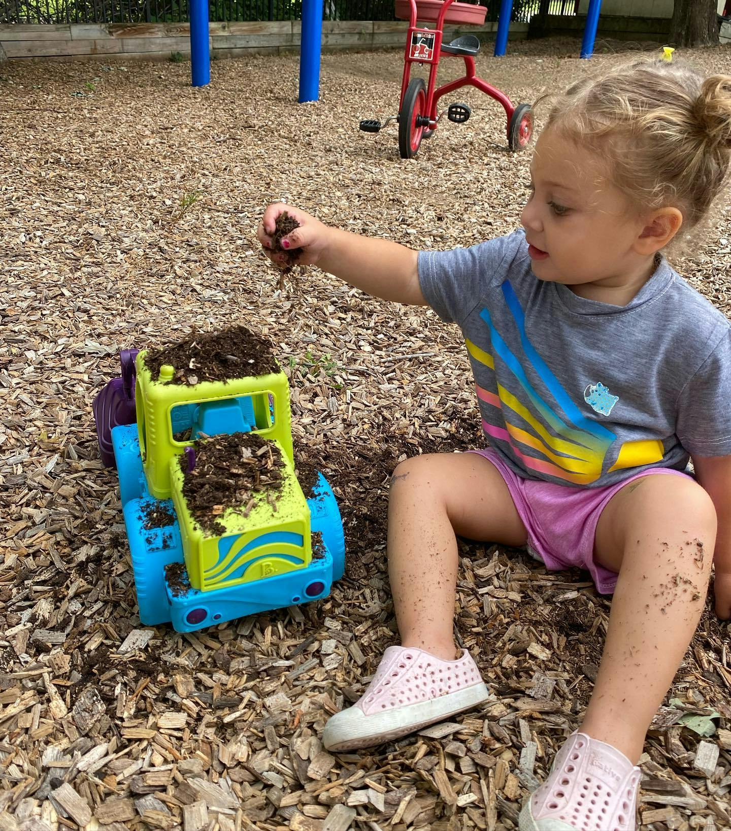 Child playing with dirt and a toy truck on wood chips