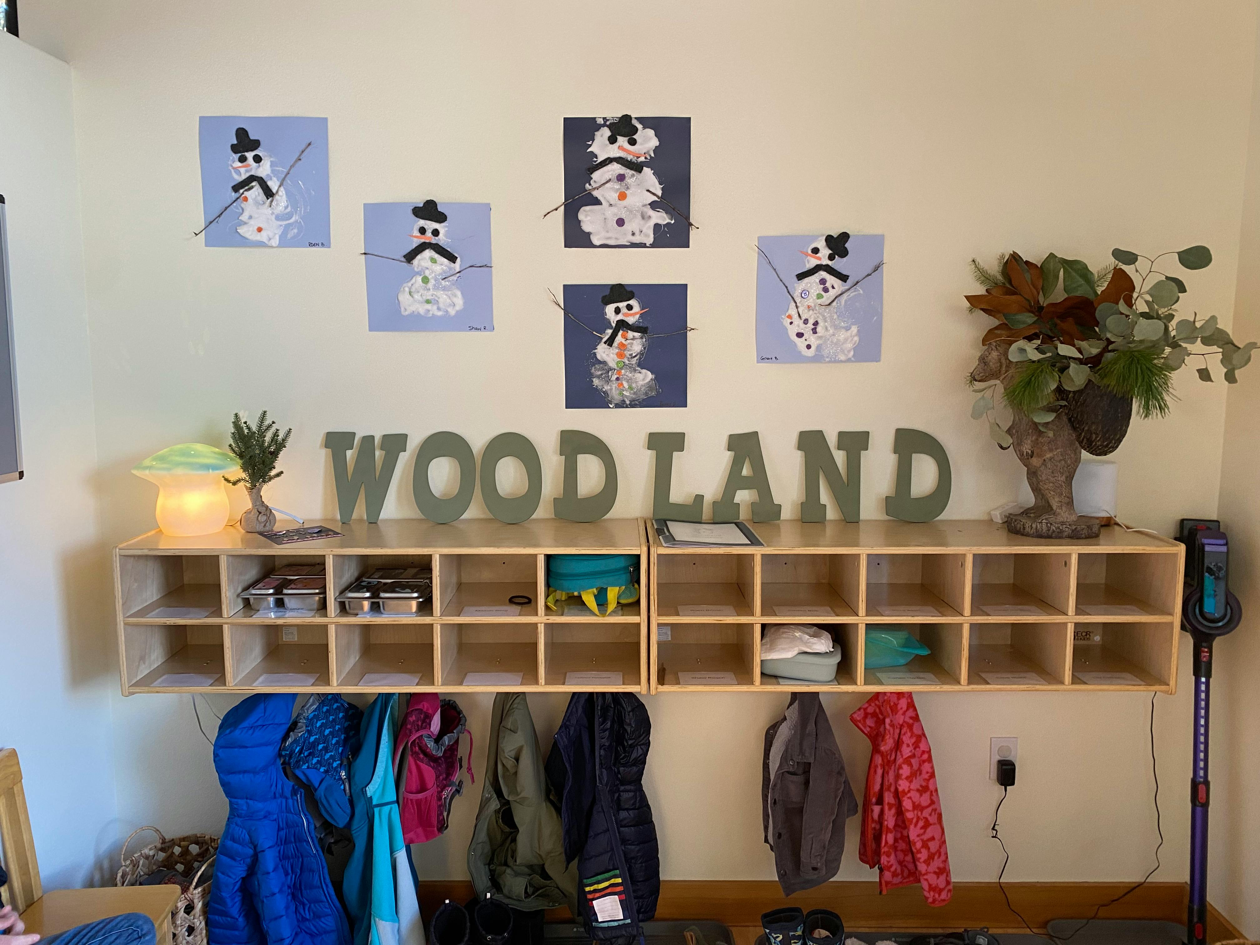 Wall with cubbies, coats, and snowman artwork, with "WOODLAND" text
