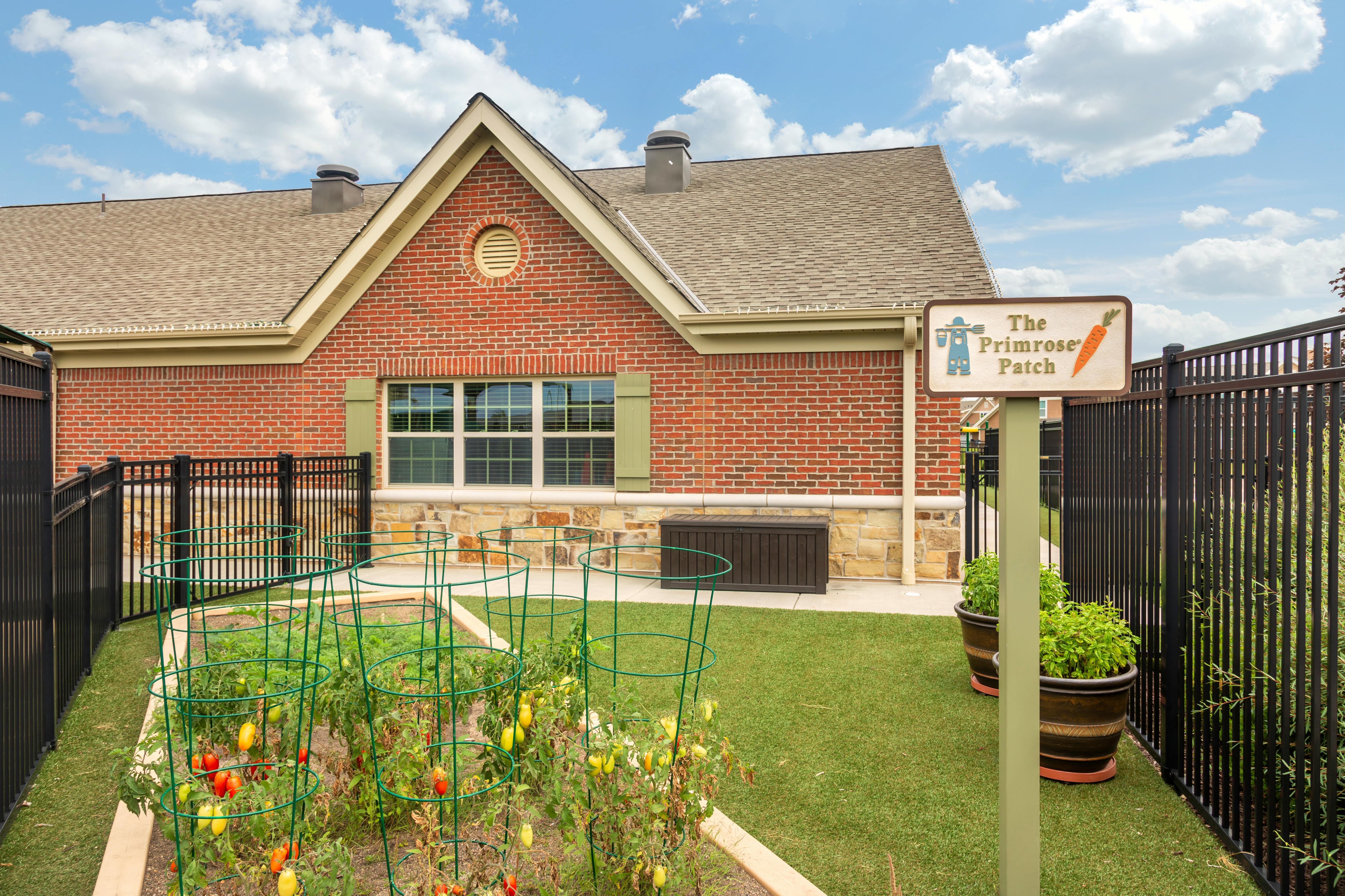 An outdoor garden with a sign reading 'The Primrose Patch' in front of a building